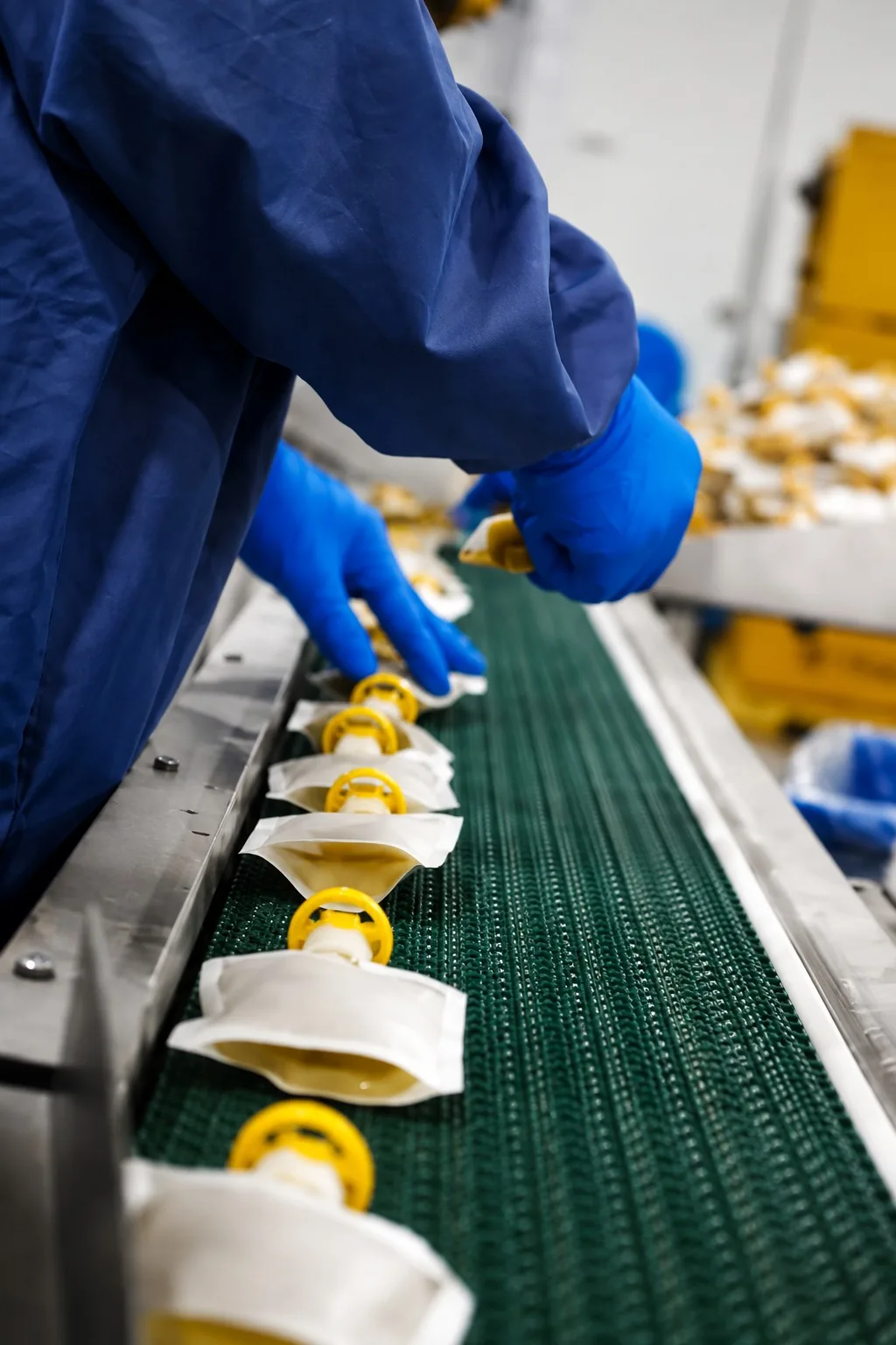 Worker sorting unbranded white squeeze pouches with yellow caps on a food production conveyor